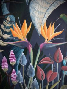 This is a close up of a section of a floral design that Becky has created. There is a green bird in the upper right hand corner. Colour theme is mainly dark colours, different shades of blue, maroon, red and purples. Two yellow flowers are central.